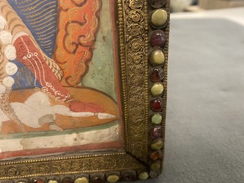 A Tibetan thangka in inlaid gilt brass frame, 19th C.
